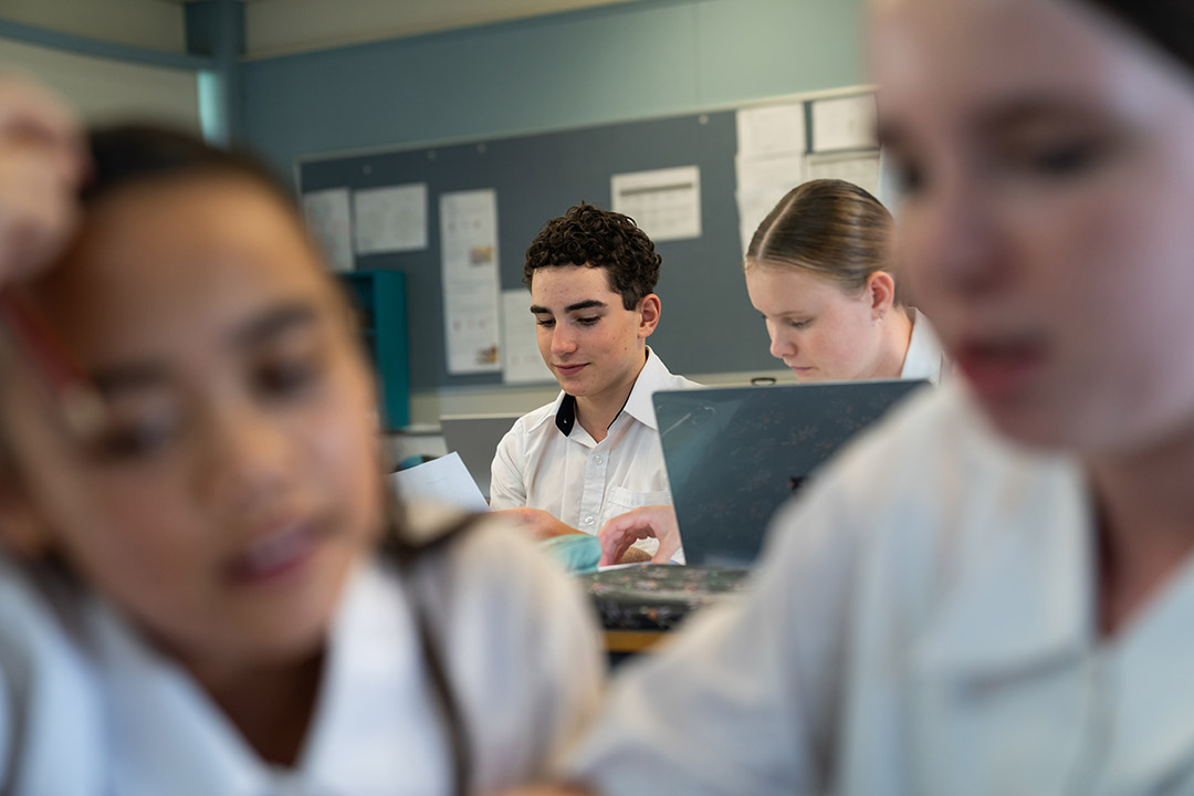 Four students seated in a classroom. Two students in the front row blurred and 2 students in the back row in focus. 