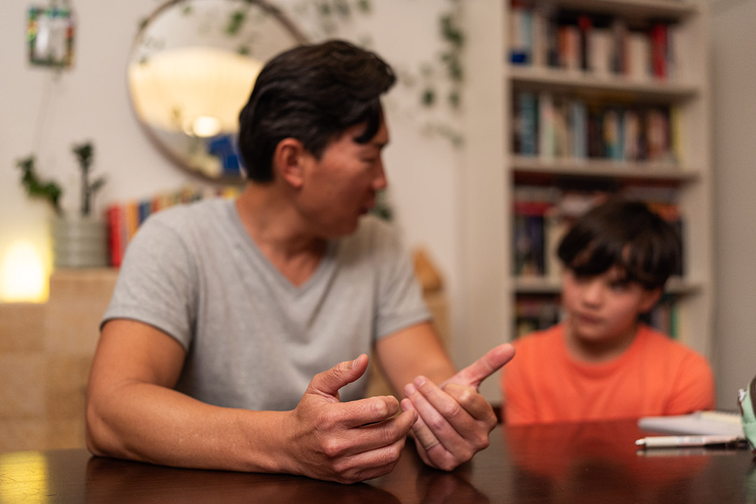 A father and child seated at a table chatting. Their faces are out of focus.