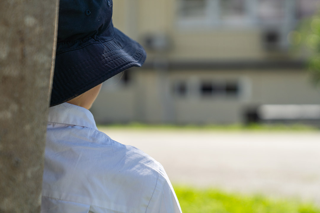A student in uniform sitting against tree looking away. 