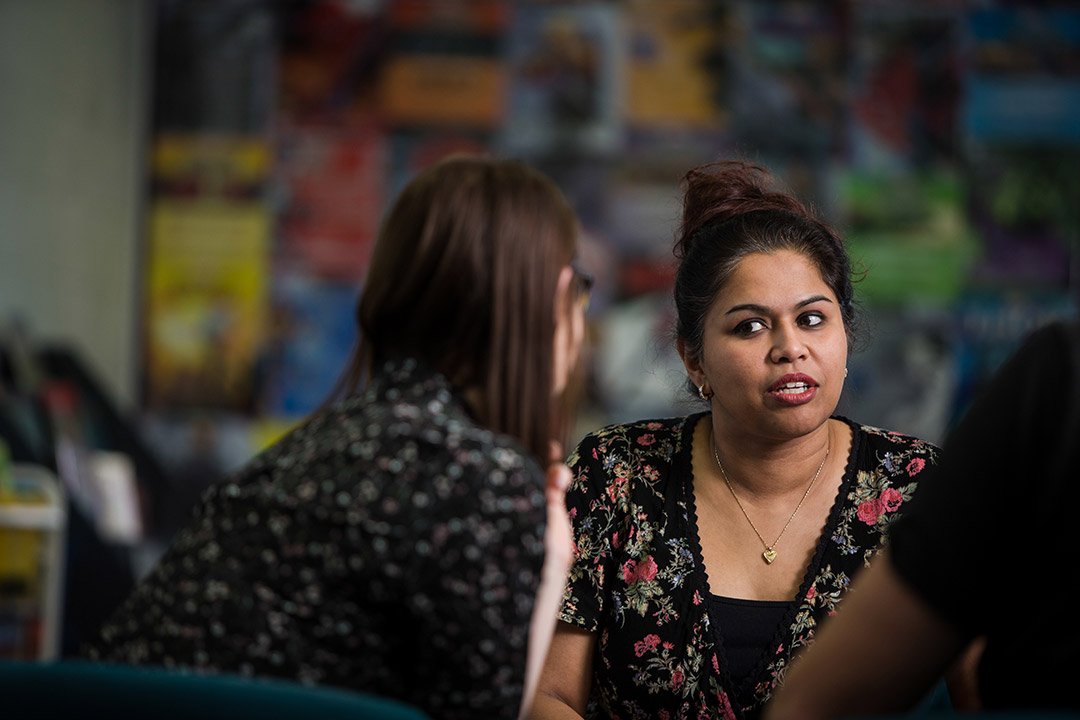 Two women in a classroom talking to each other. One facing the camera, looks concerned.
