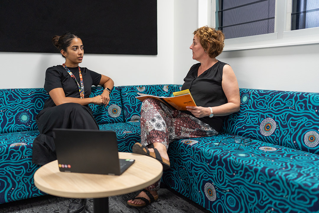Two women sitting in a staff room with a laptop and planning books.