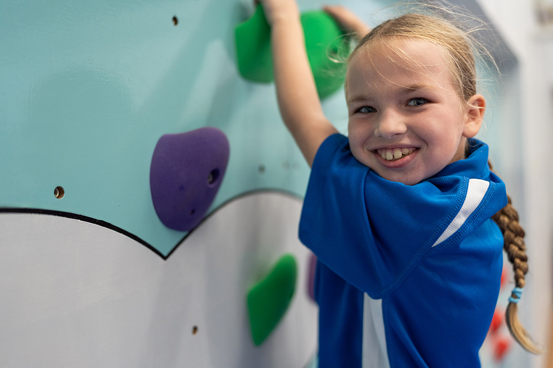 A student on a climbing wall, smiling to the camera