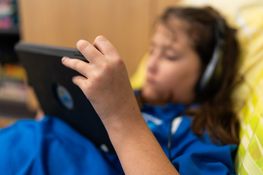 A student looking at a tablet device while sitting on a bean bag with headphones on.