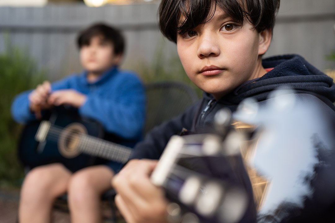 Two young children seated playing the guitar. The student in the back is slightly blurred. 