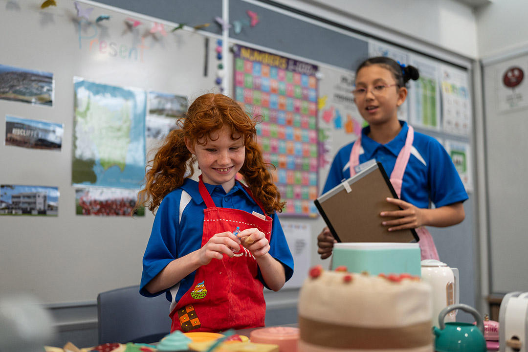 Two students wearing school uniform and a apron standing in a classroom