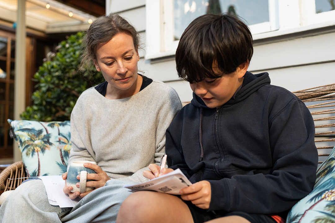 A parent sitting with her child and watching them write.