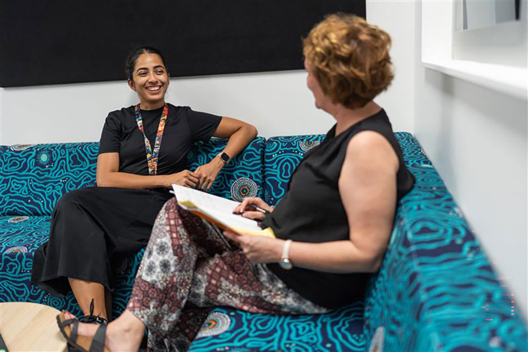 Two teachers sitting on a couch, smiling and discussing some paperwork.
